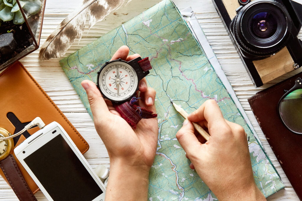 Bilde av et kart, en jentehånd med et kompass, et kamera og en mobiltelefon. Vinterturtips nummer 2 er å planlegge turen godt.